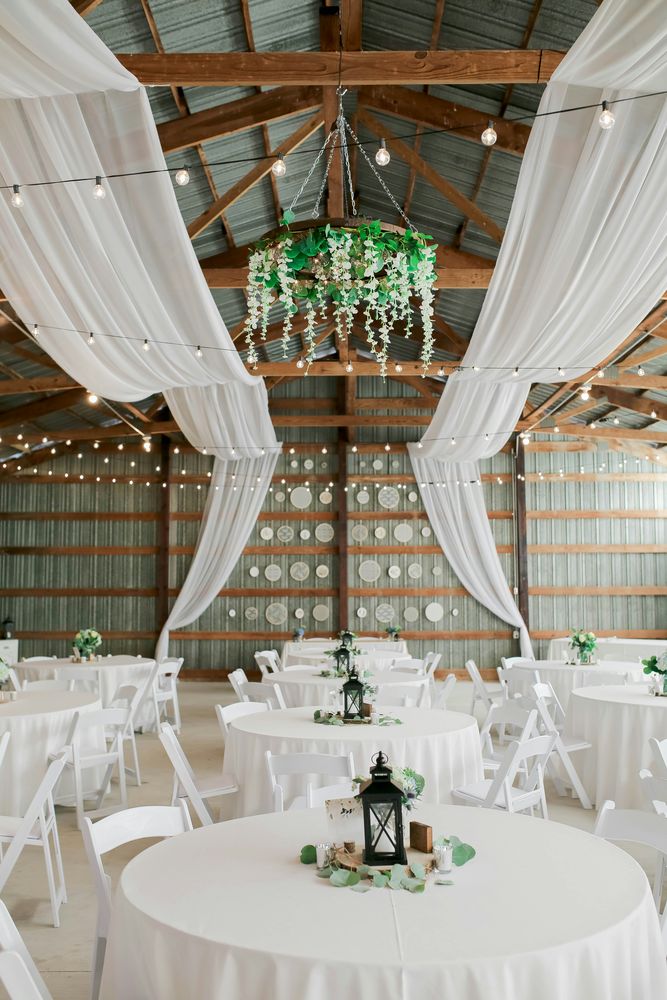A draped barn venue set with round tables and white folding chairs